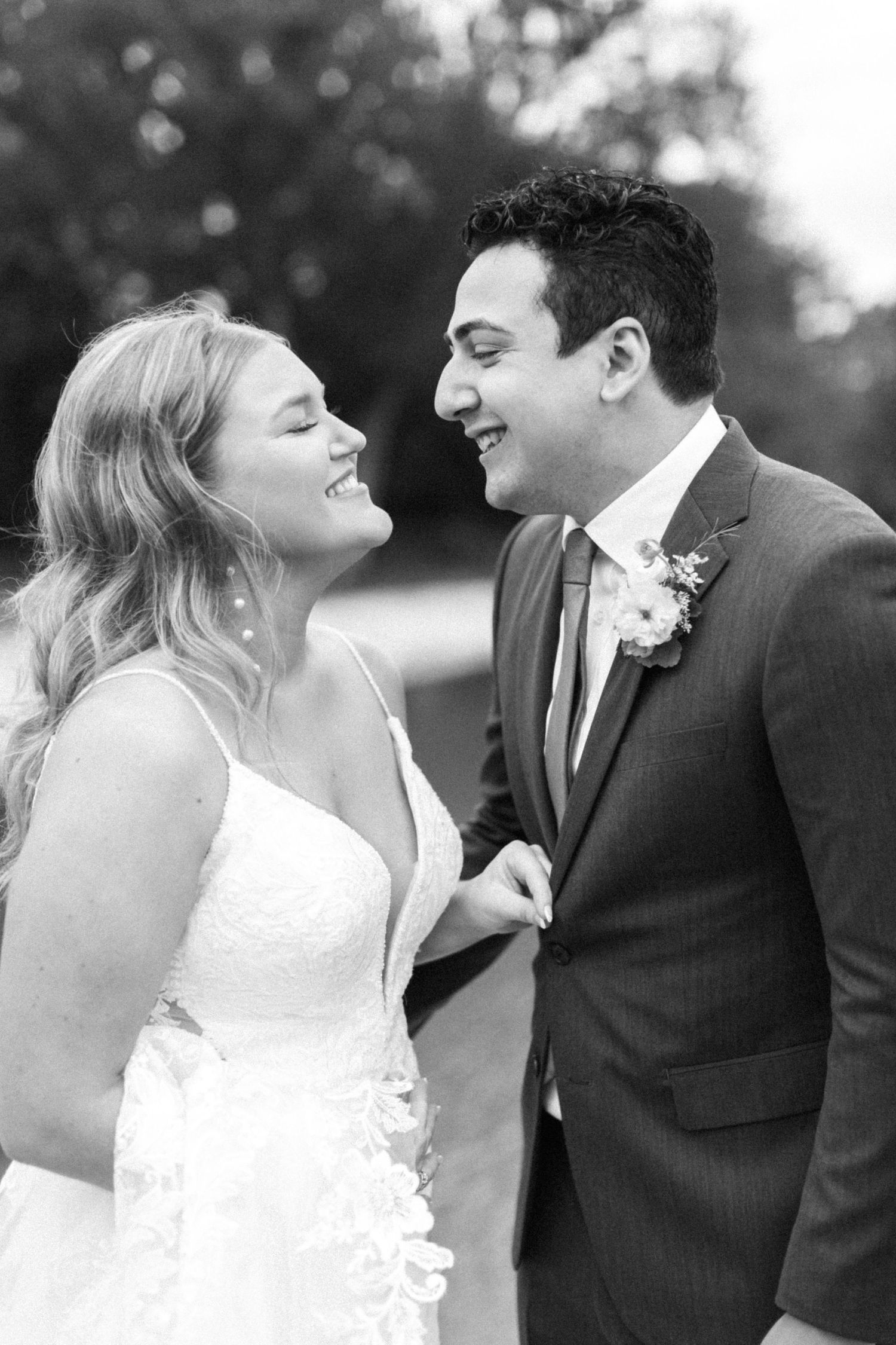 Black and white photo of a joyful wedding couple sharing a candid moment outdoors.