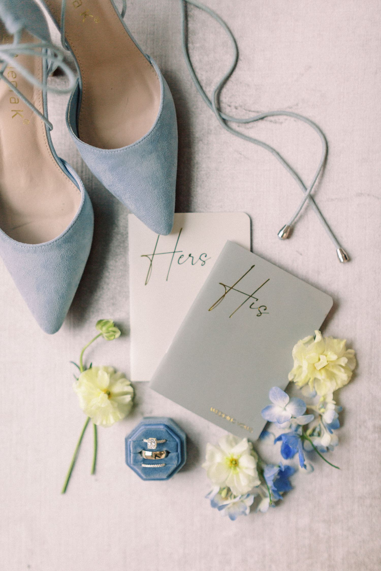Wedding details featuring blue shoes, vow books and delicate floral arrangements.