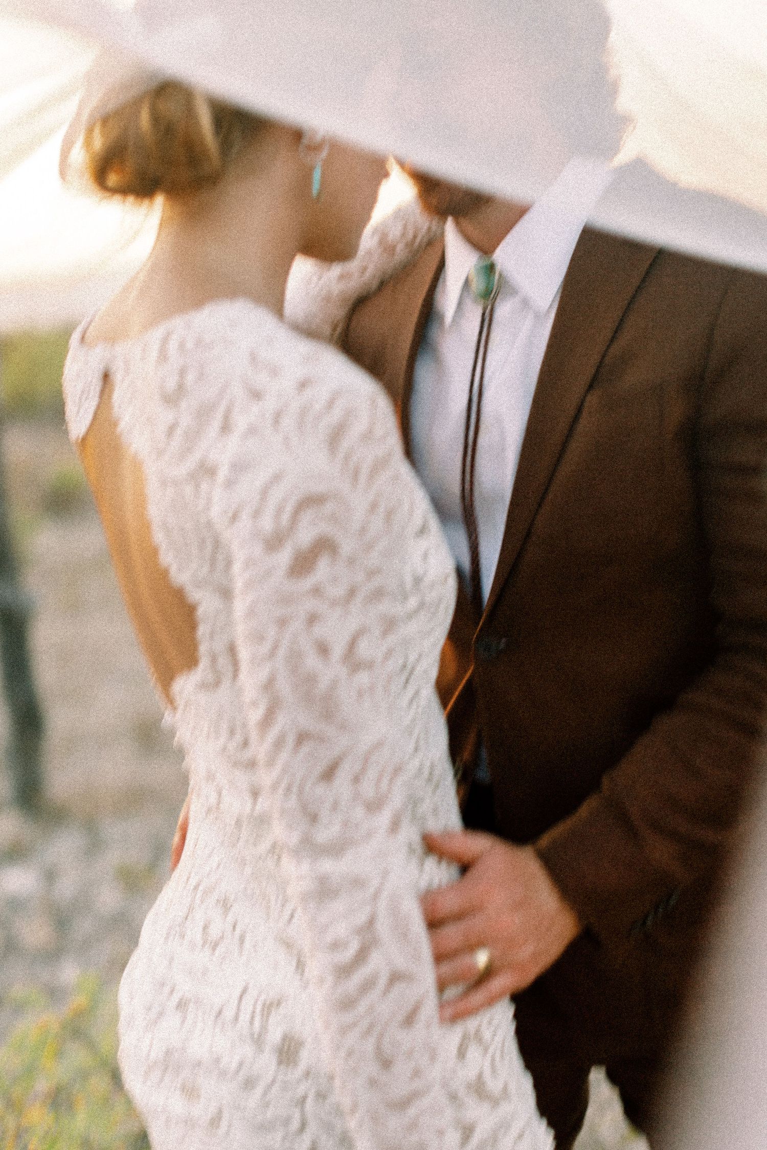 Elegant wedding couple in white lace dress and dark suit posing together outdoors.