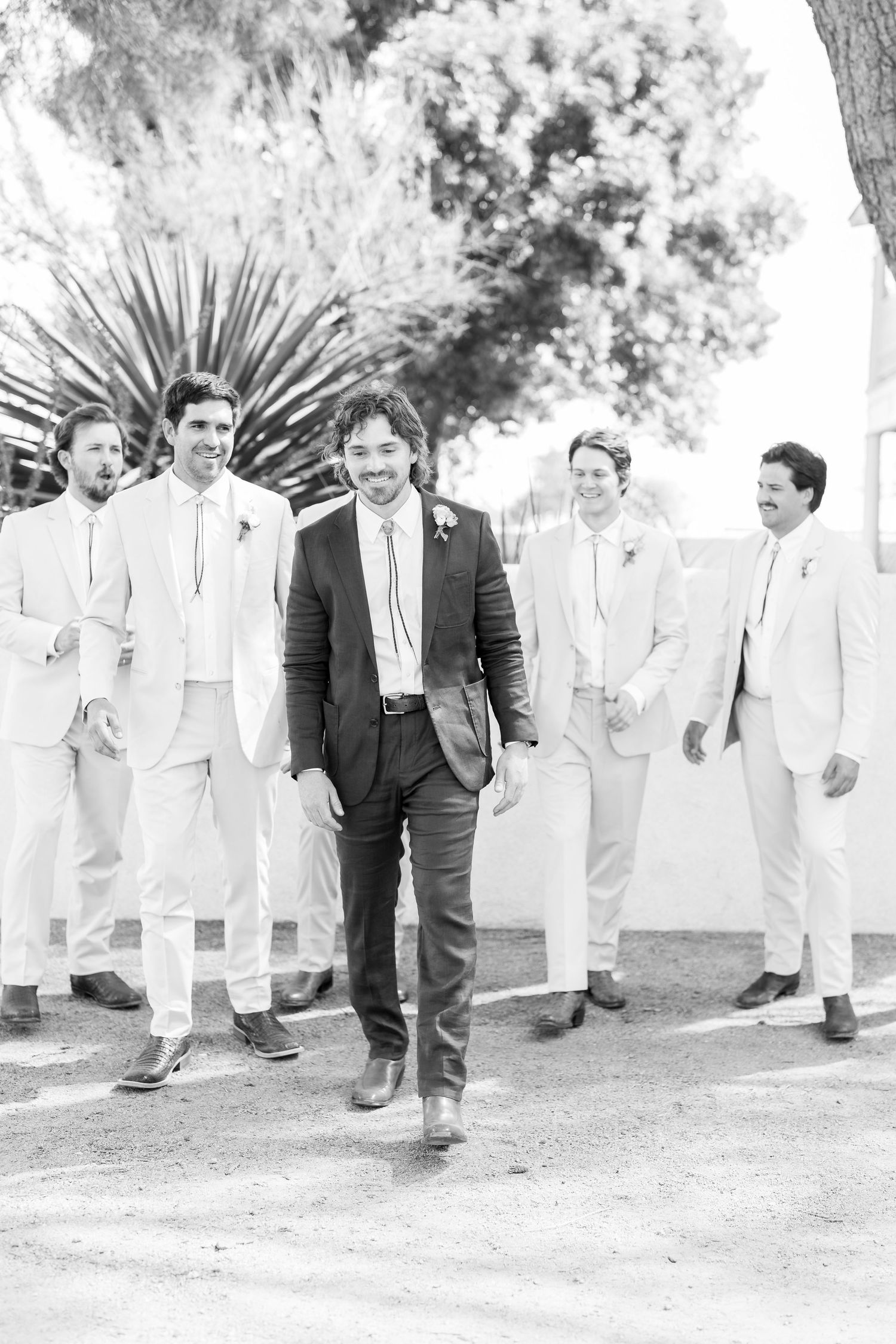Black and white photo of groomsmen in light suits walking together outdoors.