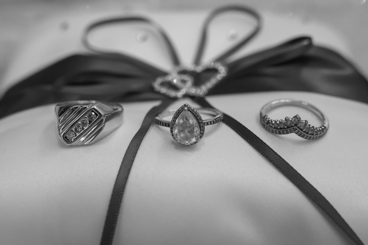Black and white detail shot of wedding rings with decorative ribbon.