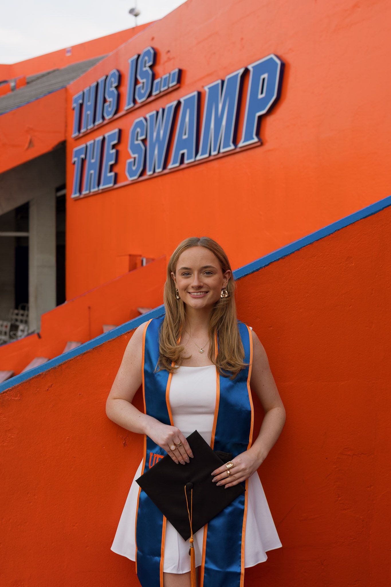 University of Florida graduate smiling in cap and gown at The Swamp stadium, holding graduation cap.