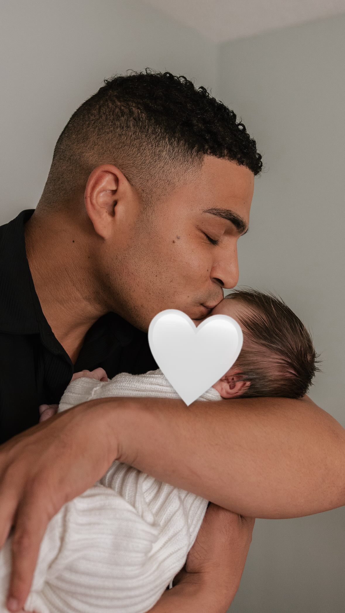 A tender moment showing a parent holding and comforting a baby in a white onesie against a neutral background.