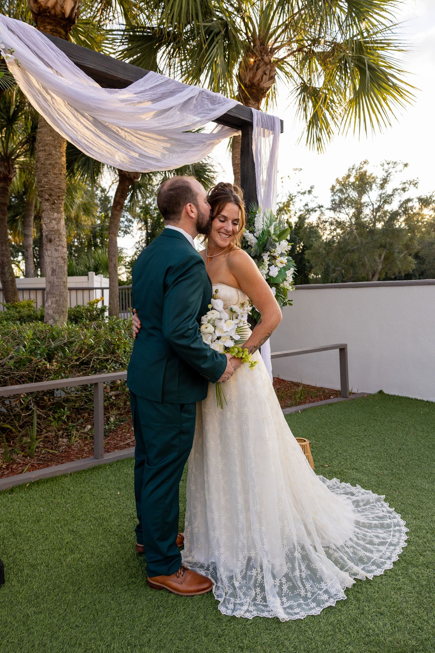 Outdoor wedding ceremony setup with palm trees and white fabric draping in a garden setting.