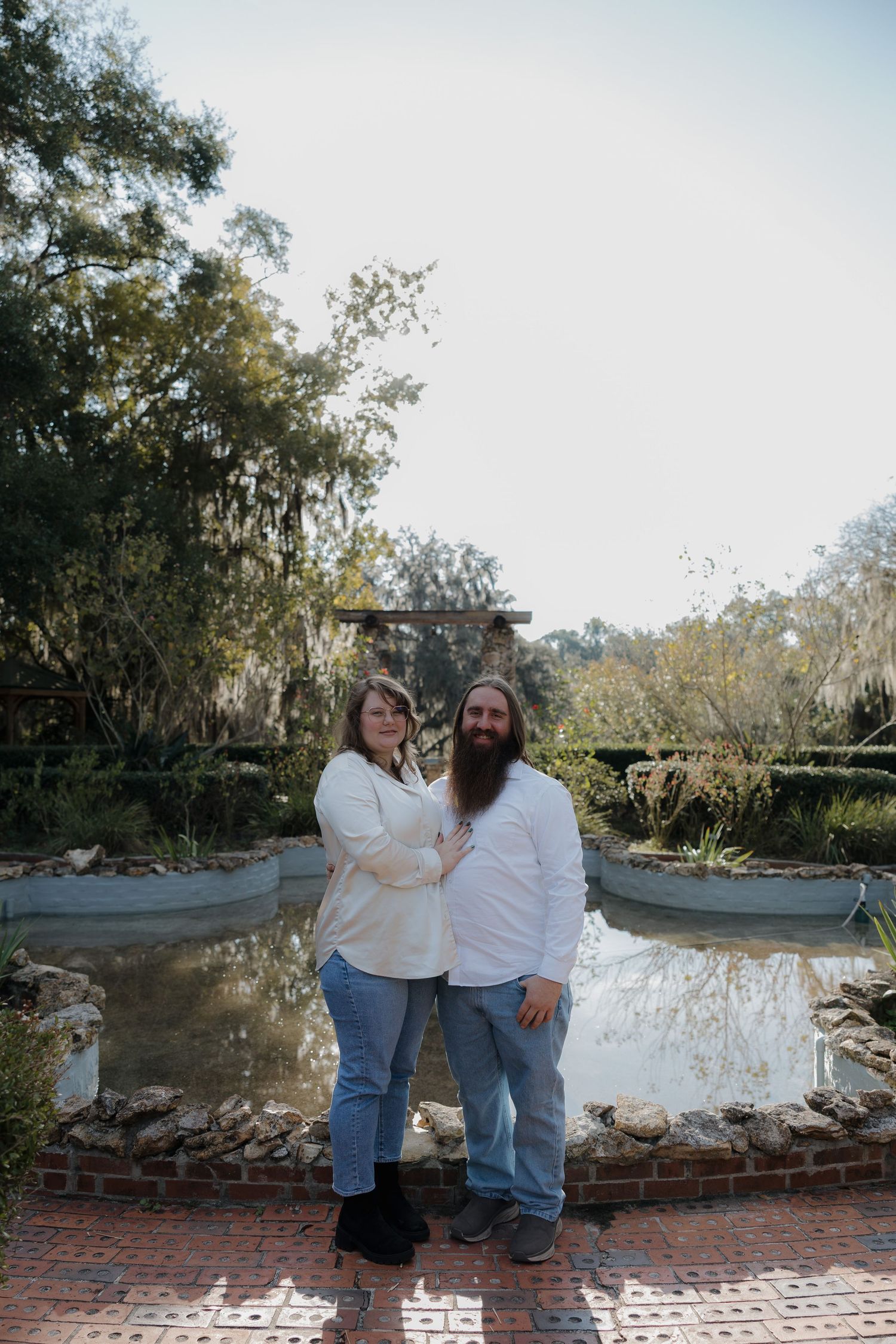 Casual couple in white shirts and jeans posing together on brick pathway.