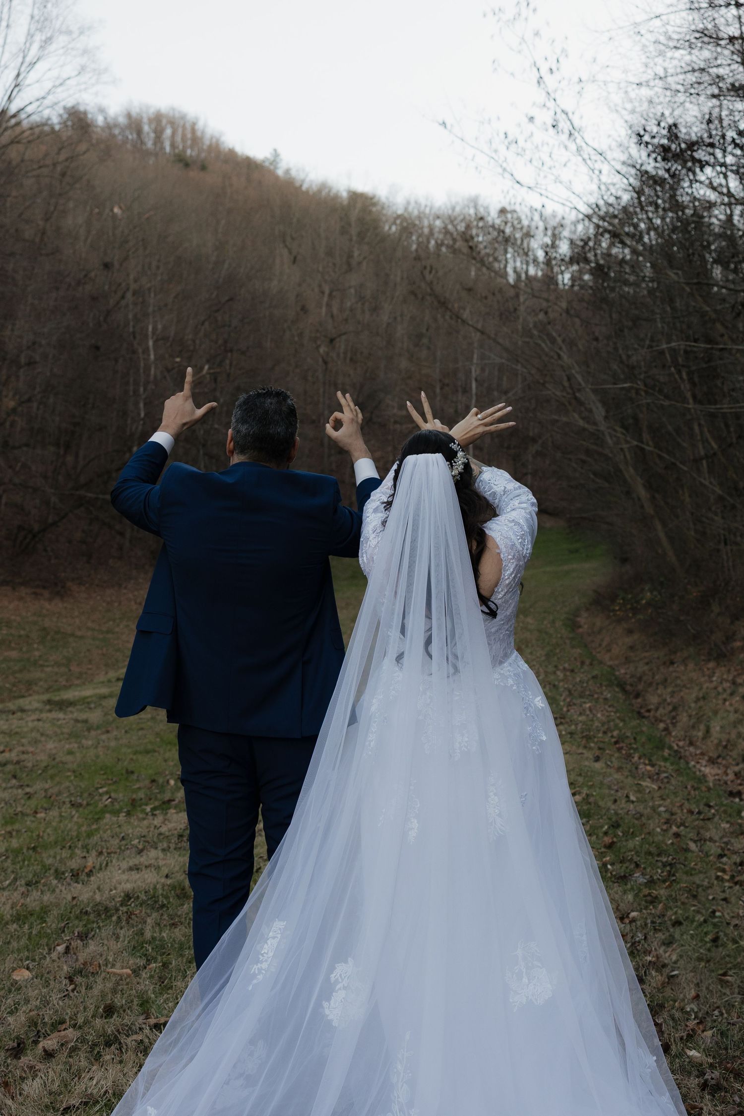 A couple in wedding attire walking away from the camera with their arms raised in a celebratory pose.