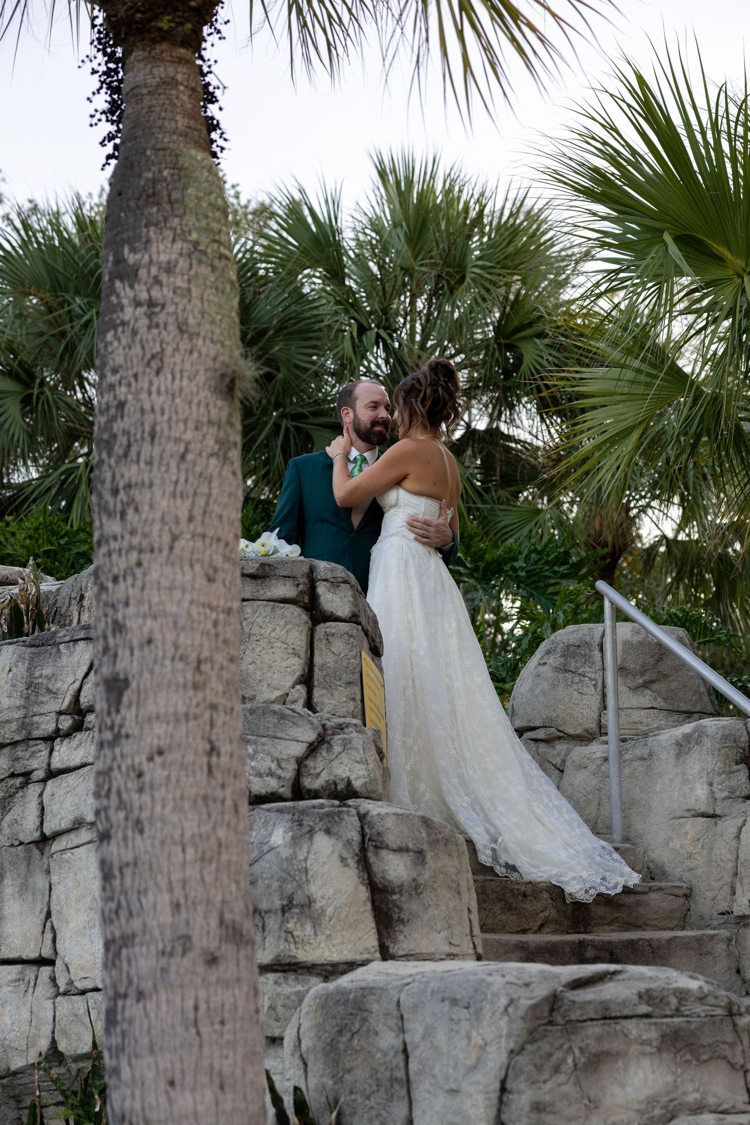 Couple posing on decorative stone steps surrounded by tropical palm trees.