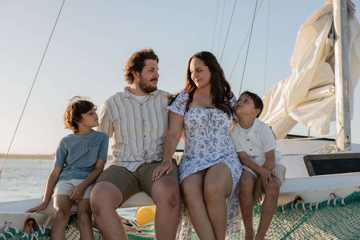 Happy family of four sitting together on a sailboat deck, enjoying a sunny day on the water.