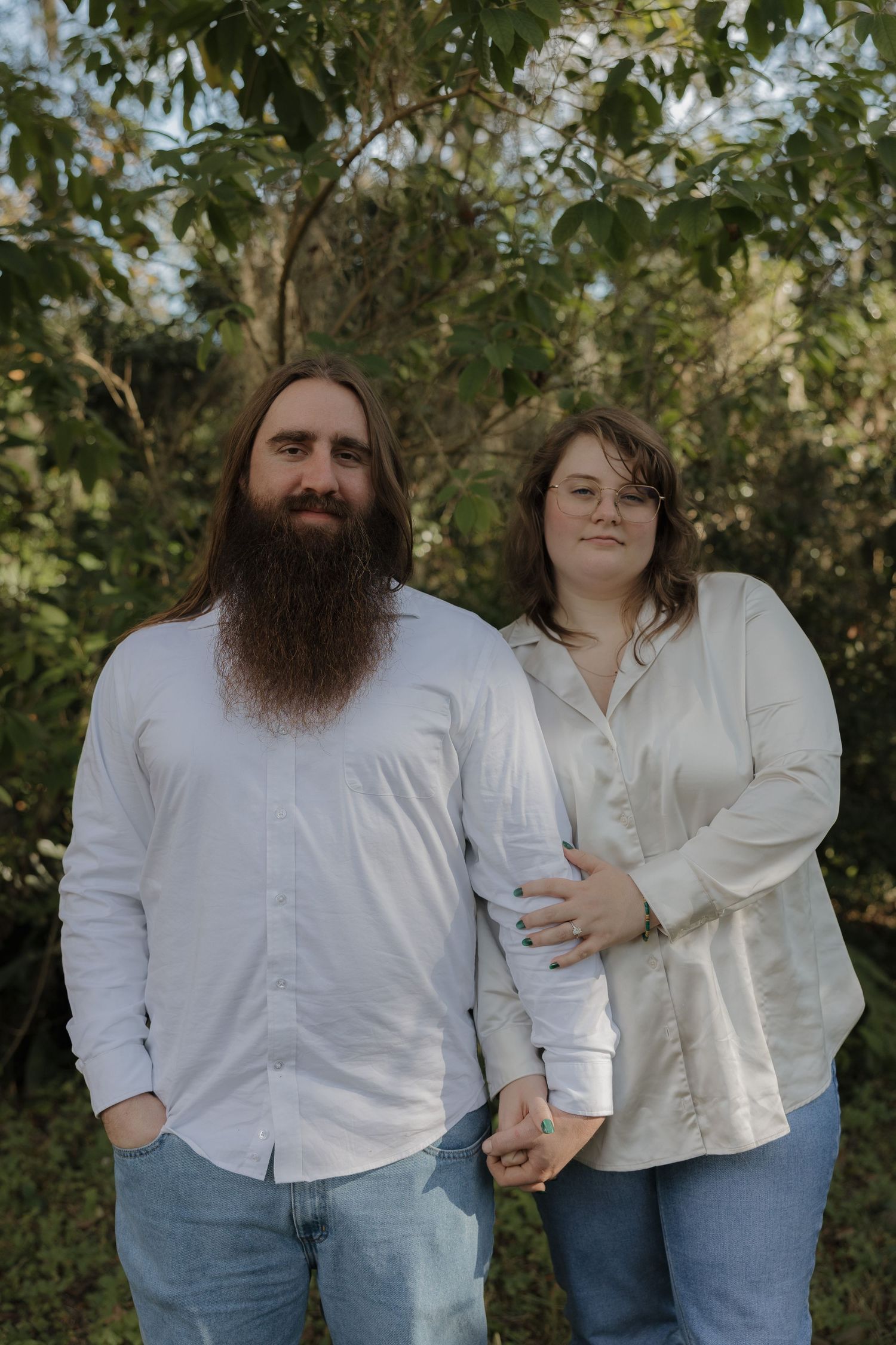 Couple in white shirts and jeans pose together in outdoor engagement photos.