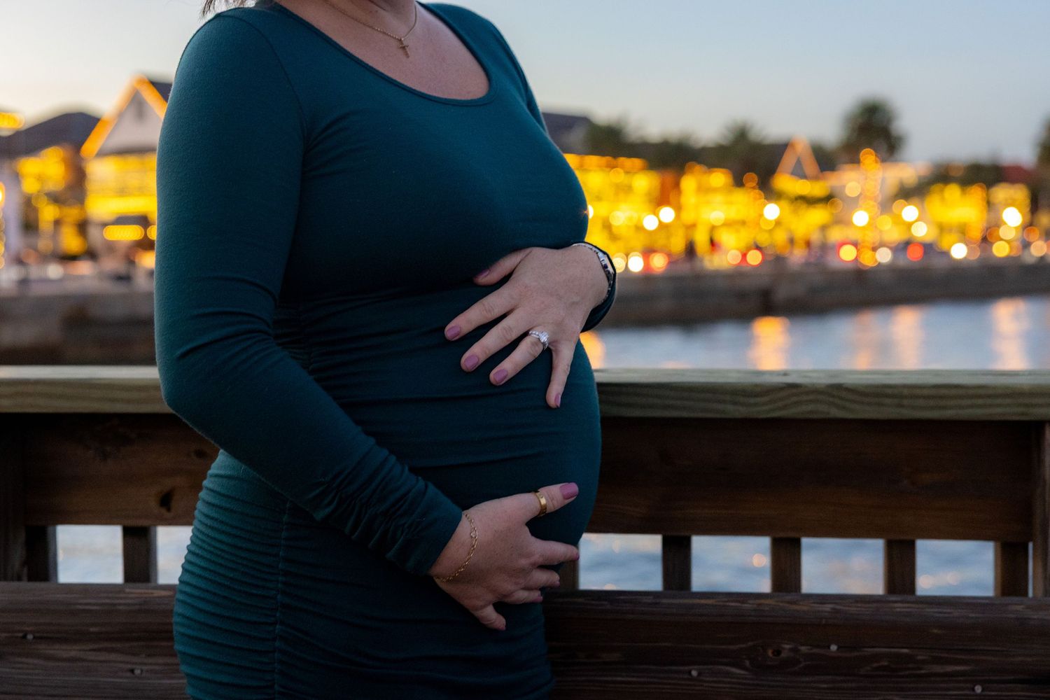 Silhouetted maternity photos at sunset by the water with city lights glowing in the background.