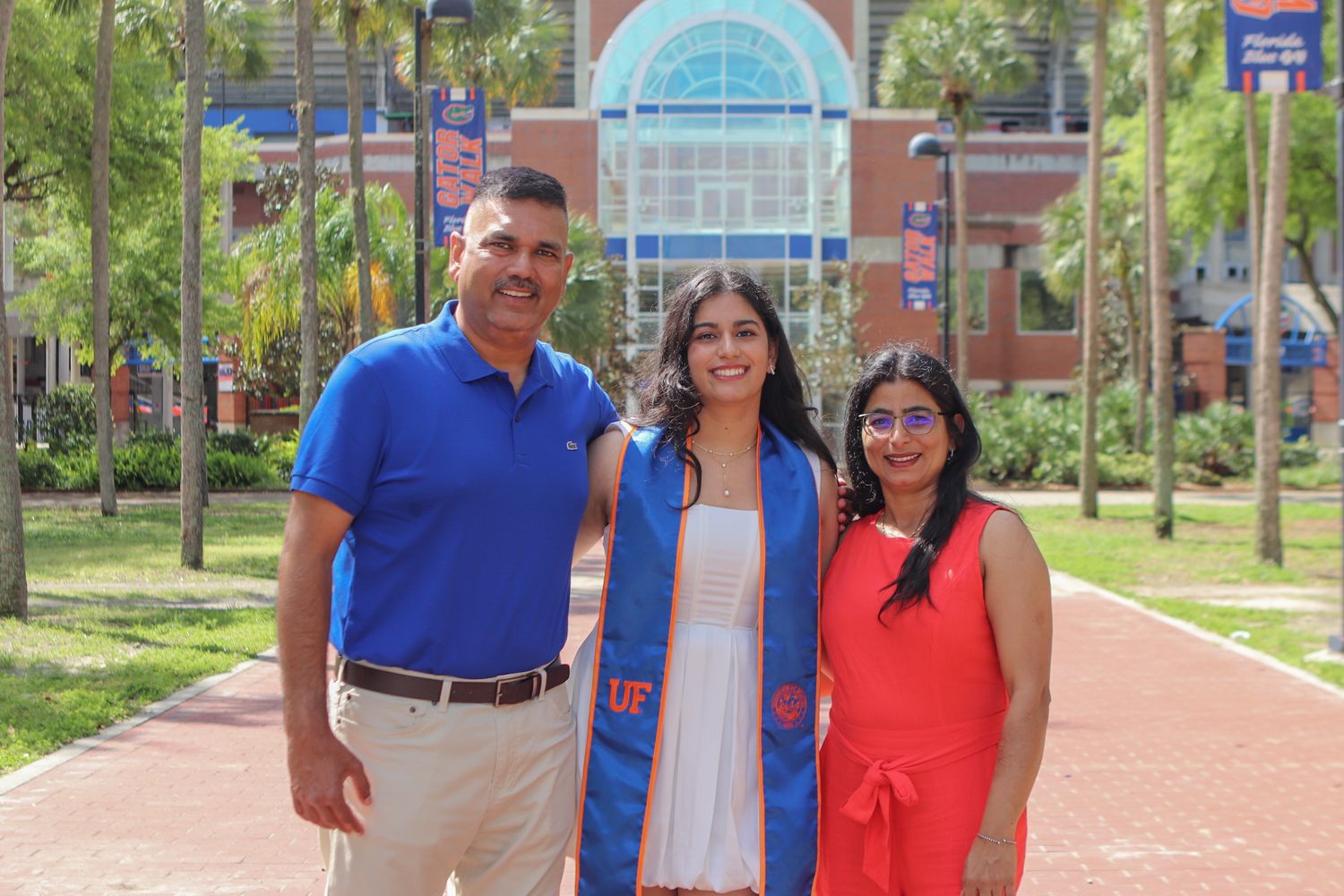Family stands together on brick pathway with palm trees and university building in background.