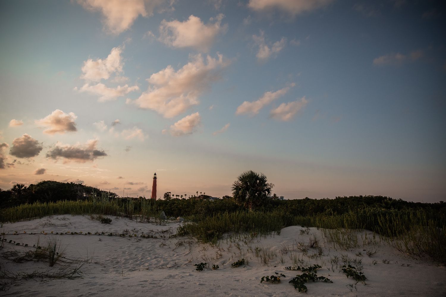 Scenic beach sunset views with sand dunes and lighthouse in the distance.