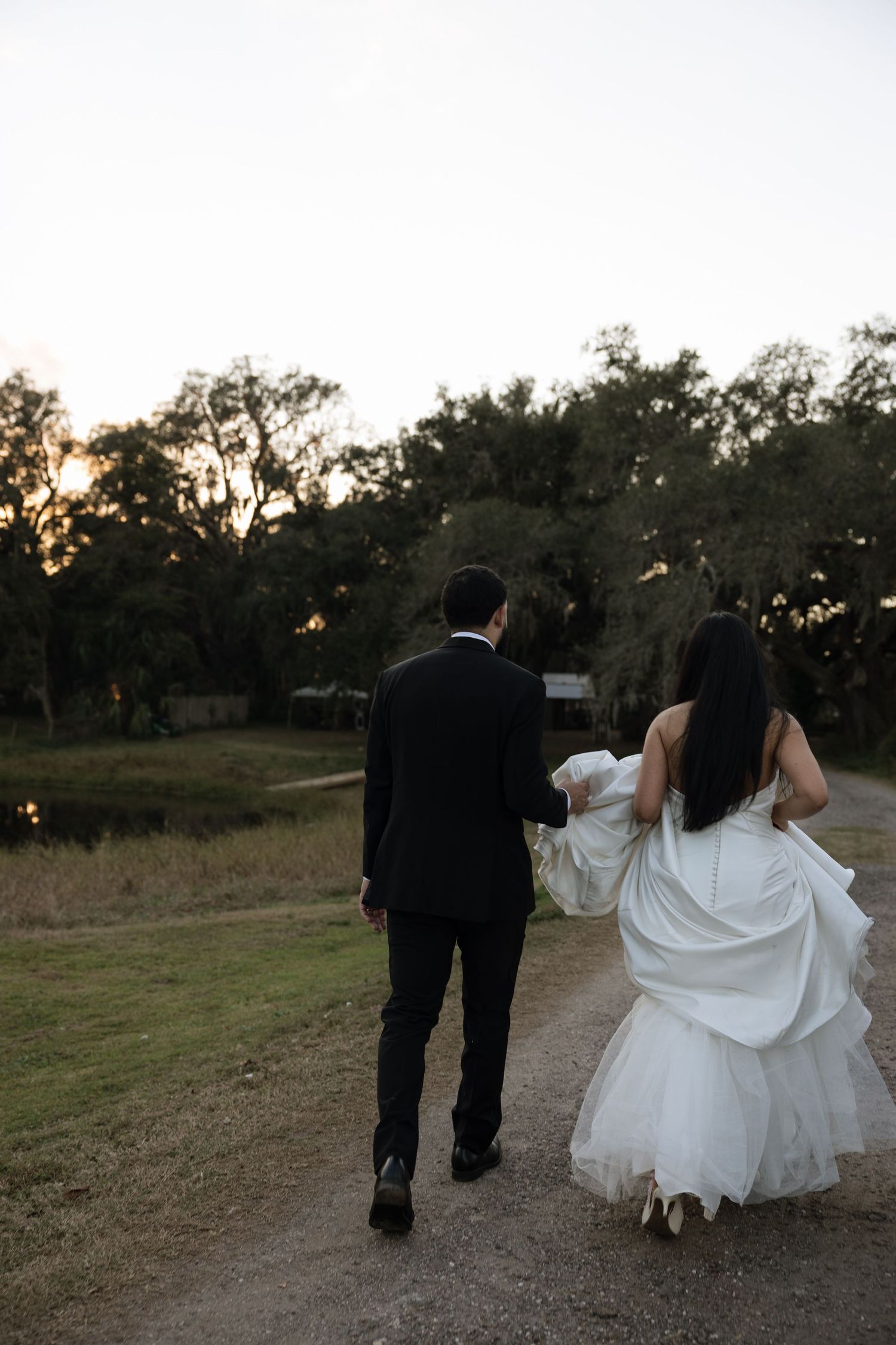 Couple walking together on a grassy path at sunset during their wedding celebration.