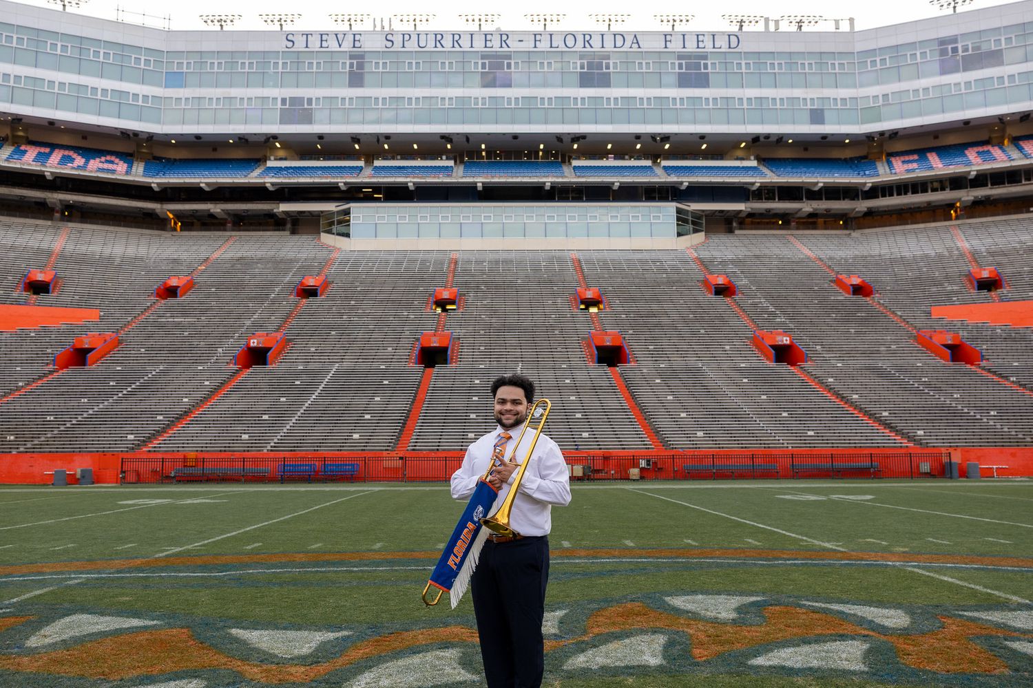Graduate in cap and gown holds trumpet on Florida Field at Ben Hill Griffin Stadium, University of Florida.