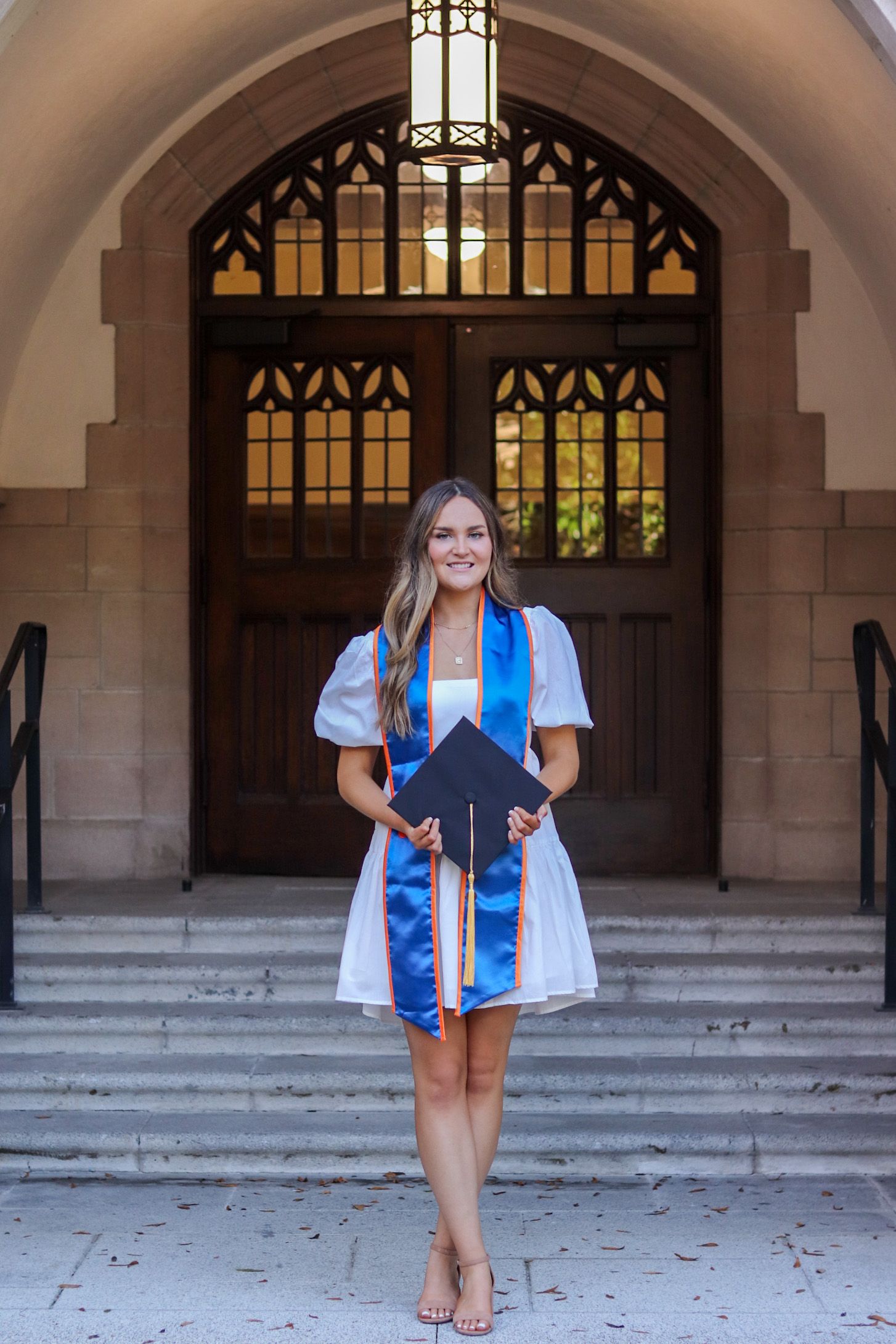 Graduate poses in front of ornate archway entrance wearing blue graduation stole.