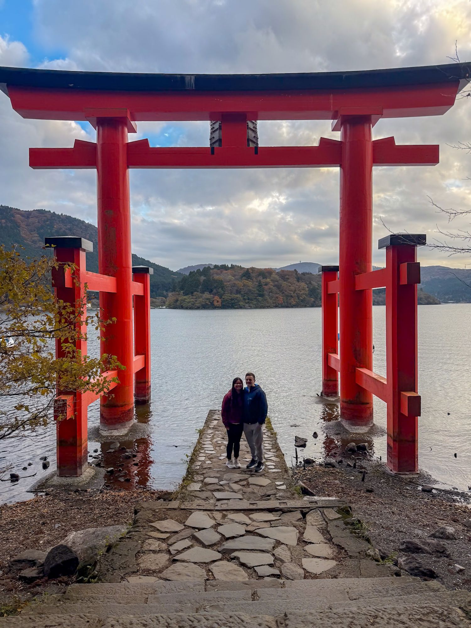 A Japanese torii gate stands in water against a cloudy mountain landscape.
