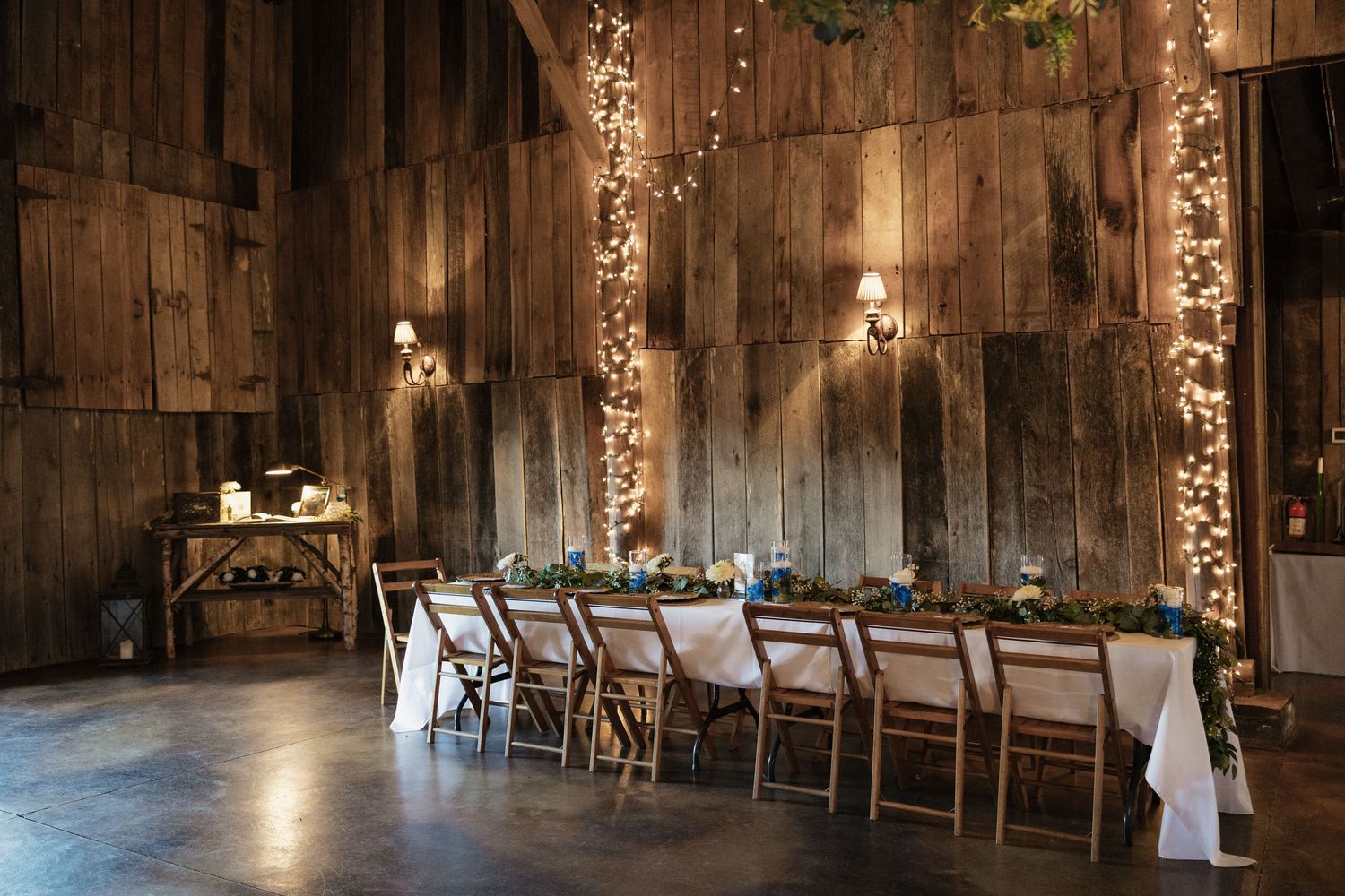 Interior of a rustic barn wedding venue with wooden beams and romantic lighting.