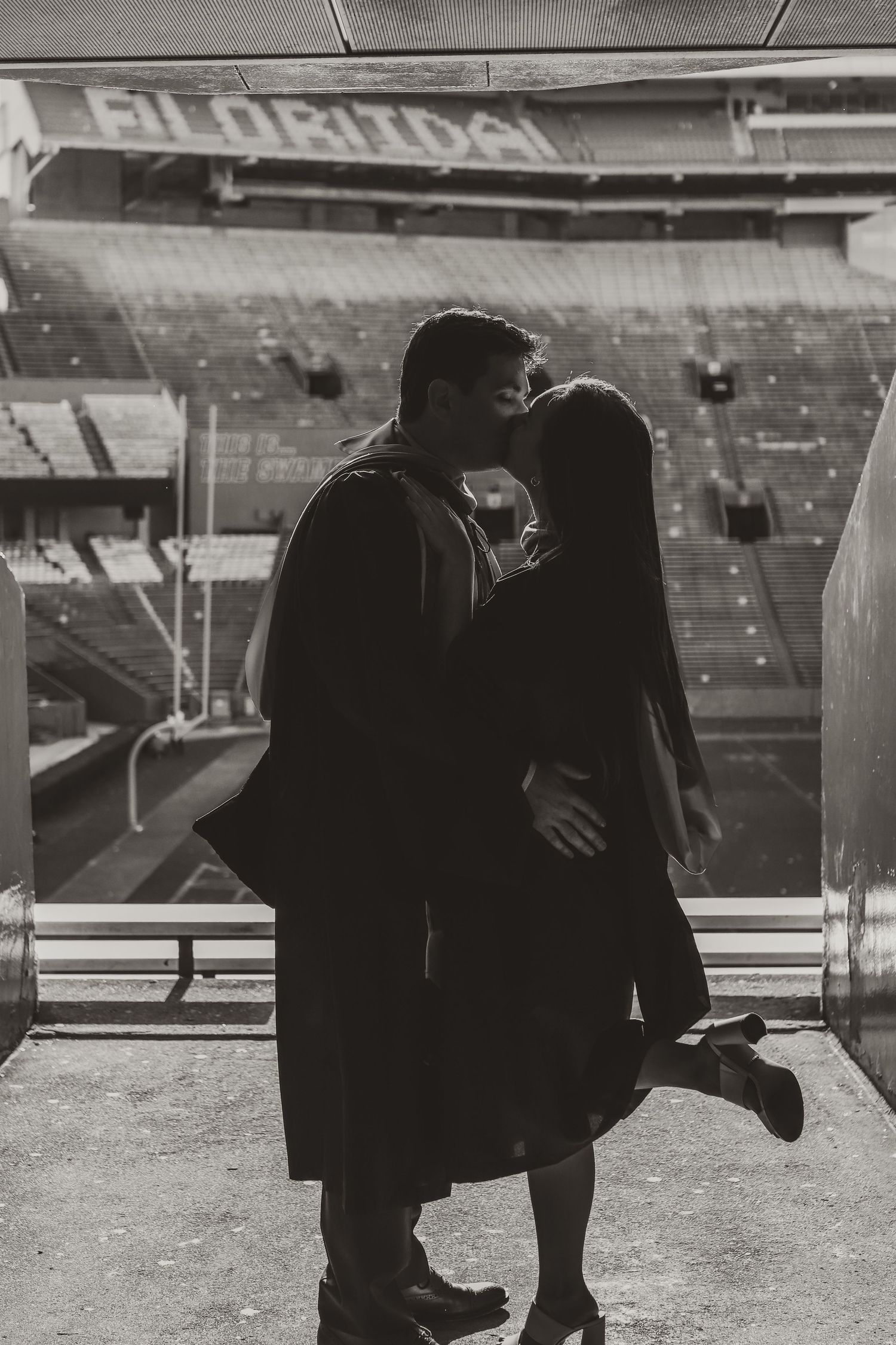 Silhouette of couple sharing romantic moment in graduation attire at stadium.