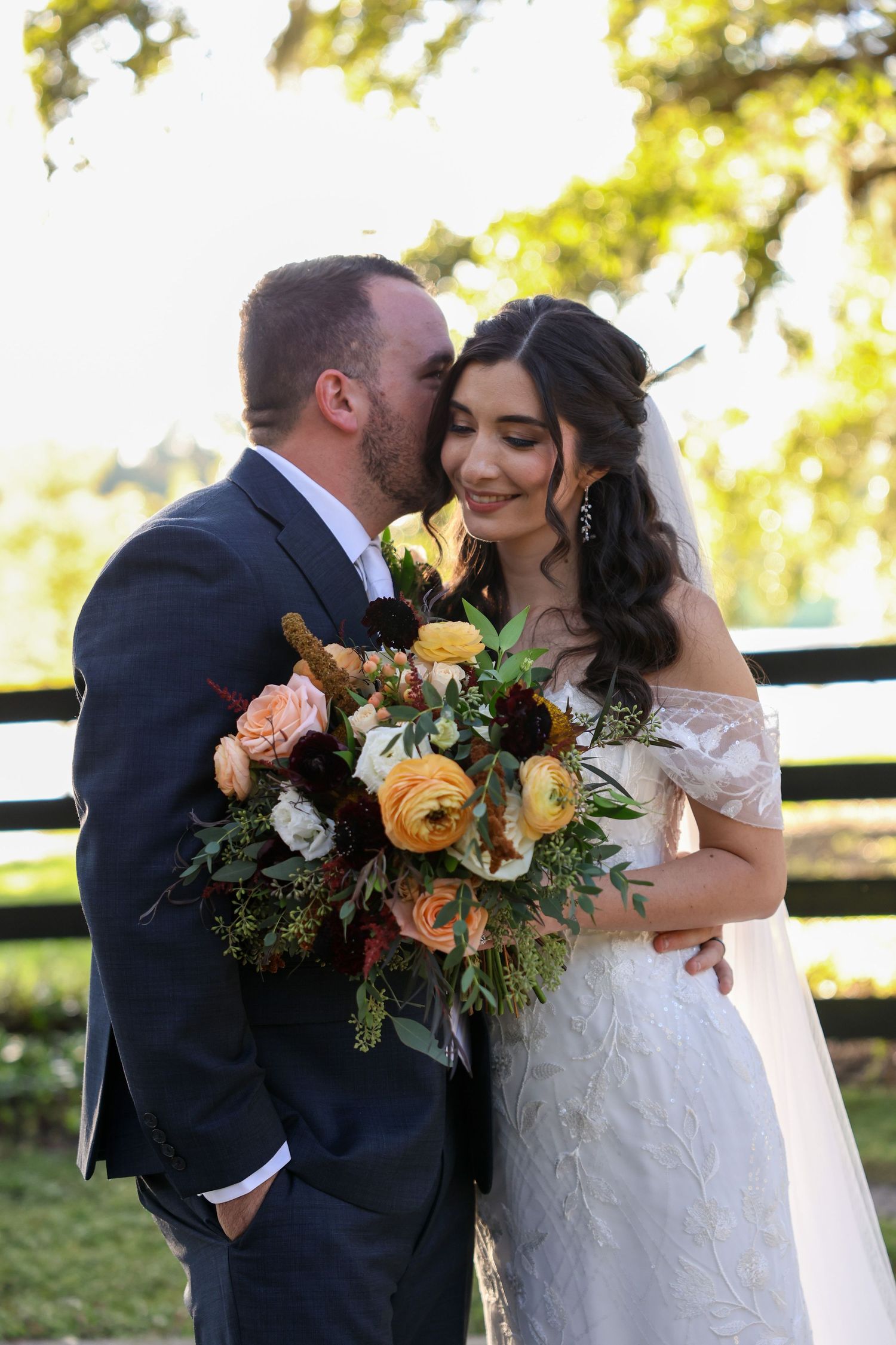 Wedding couple sharing intimate moment with orange and yellow floral bouquet in outdoor setting.