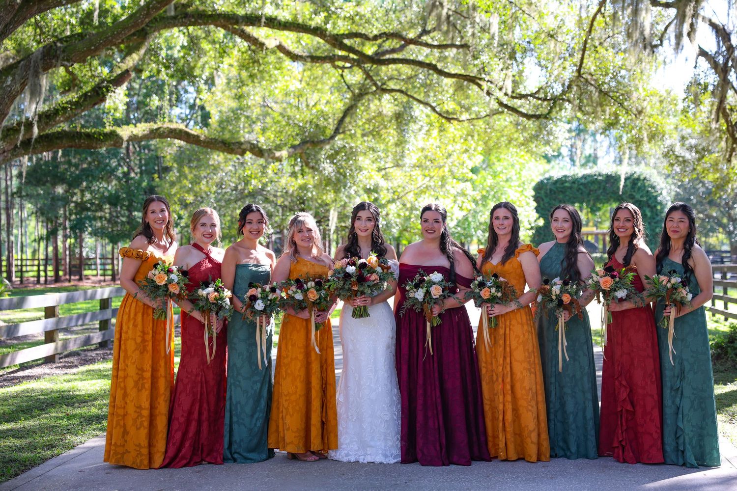 Wedding party in colorful dresses posed under oak trees.