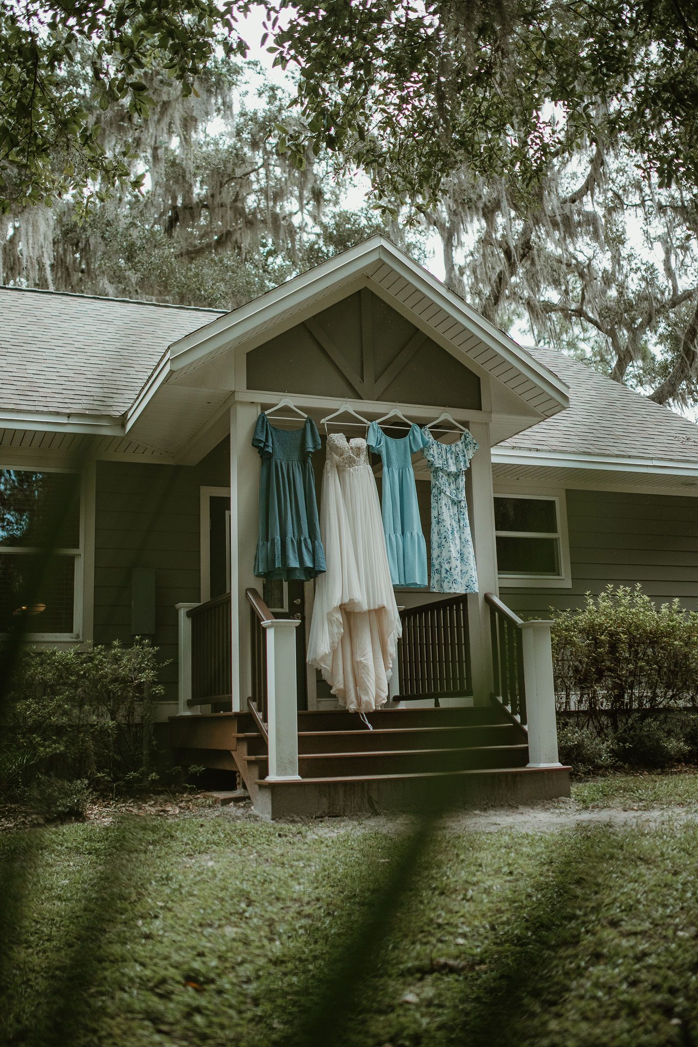 A ranch-style house with blue shutters and hanging clothes in the shade of oak trees.