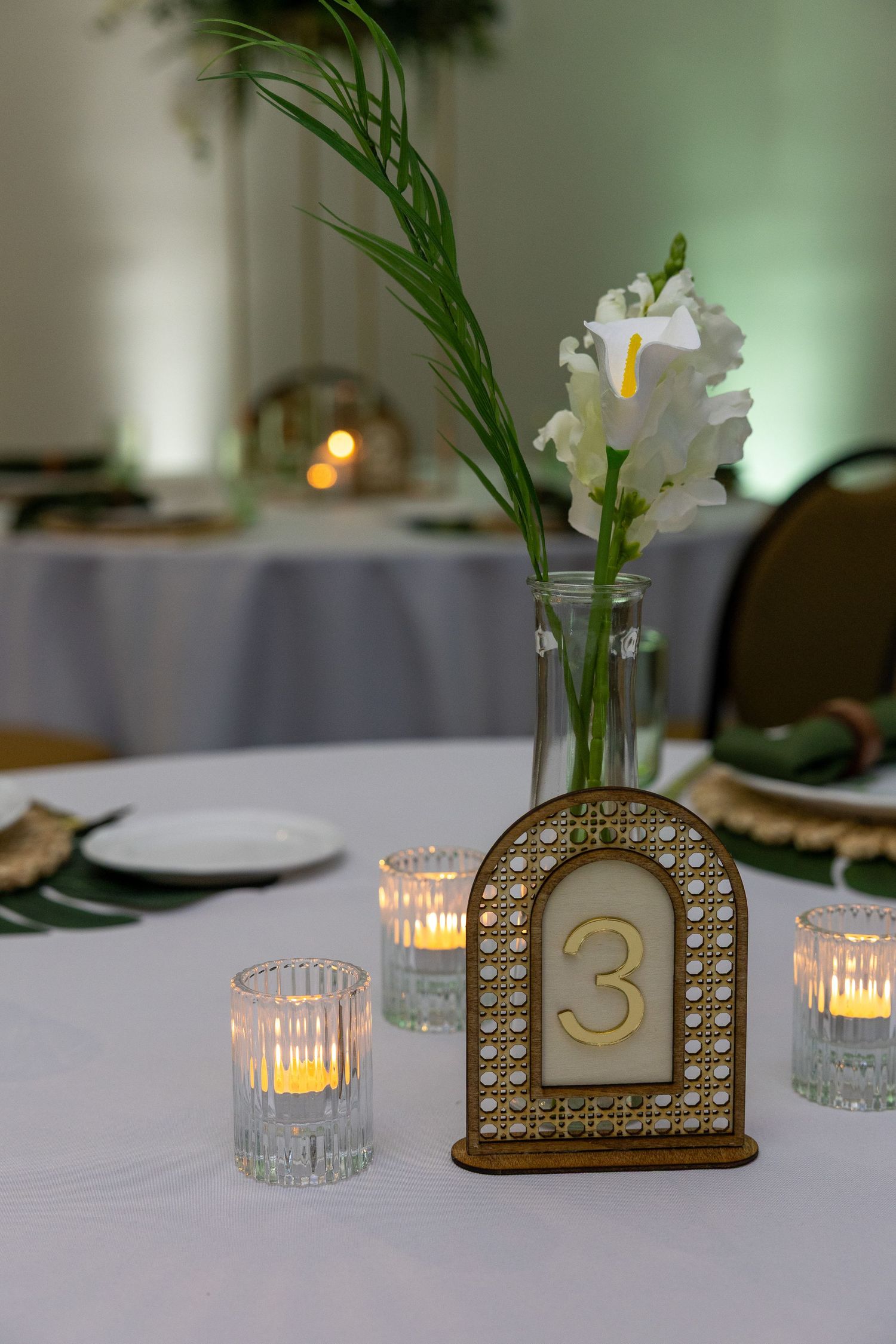 Elegant wedding table decor with illuminated candle holders and table numbers against a soft green background.