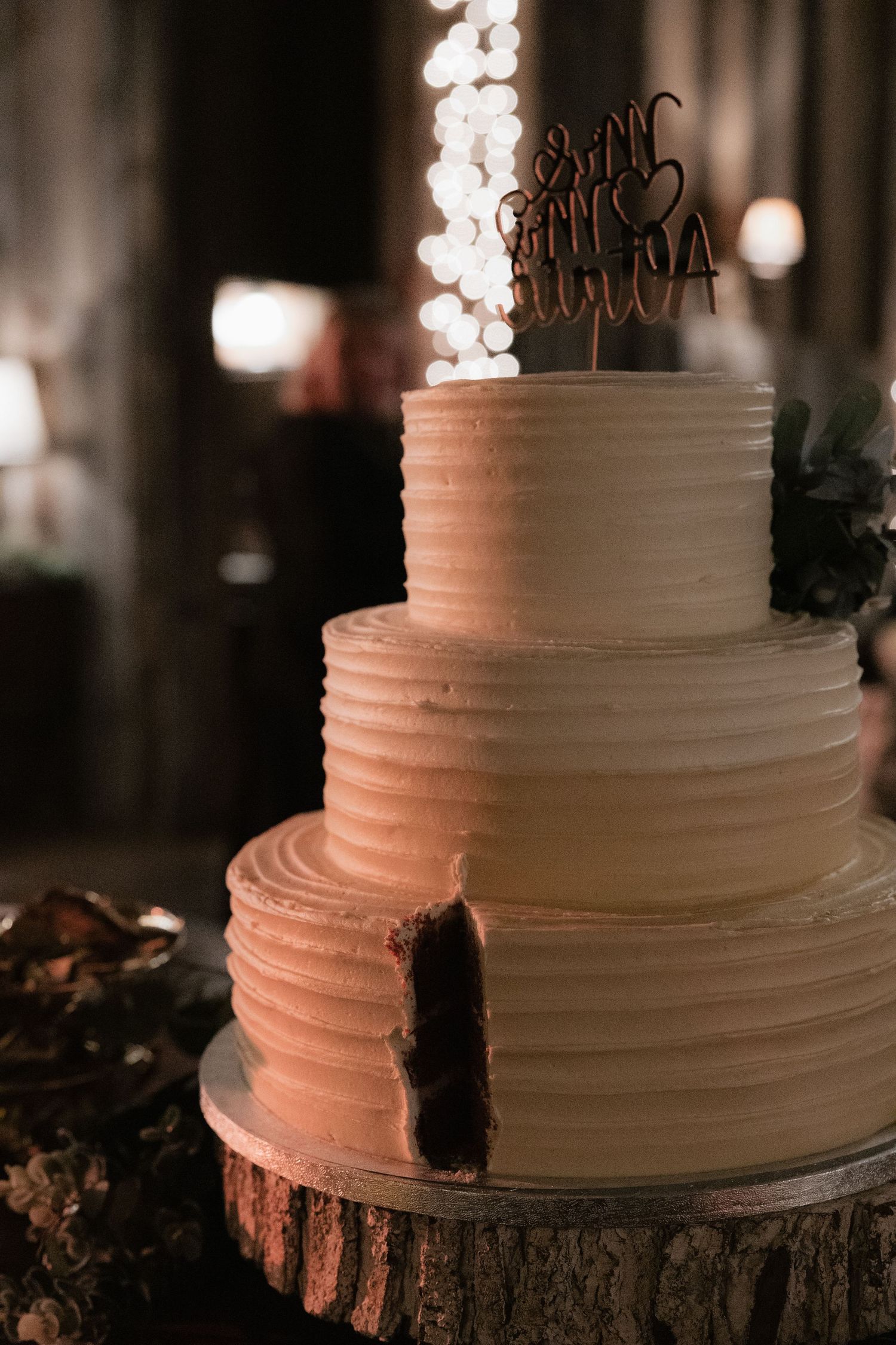 Elegant white wedding cake with textured frosting displayed on rustic wood slice stand.