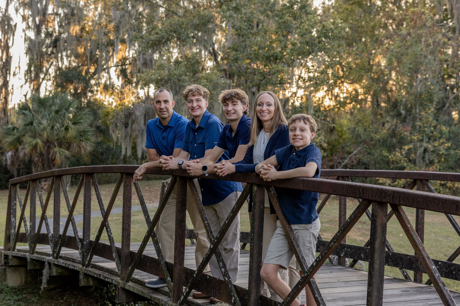 Family members stand together on a wooden bridge during an outdoor photo session.