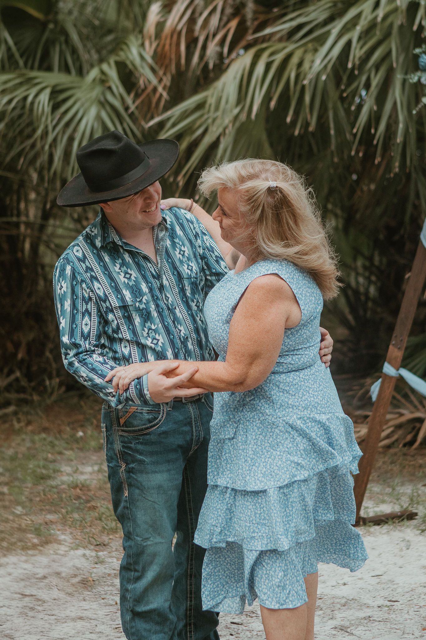 A romantic couple in western attire sharing an intimate moment among palm trees.