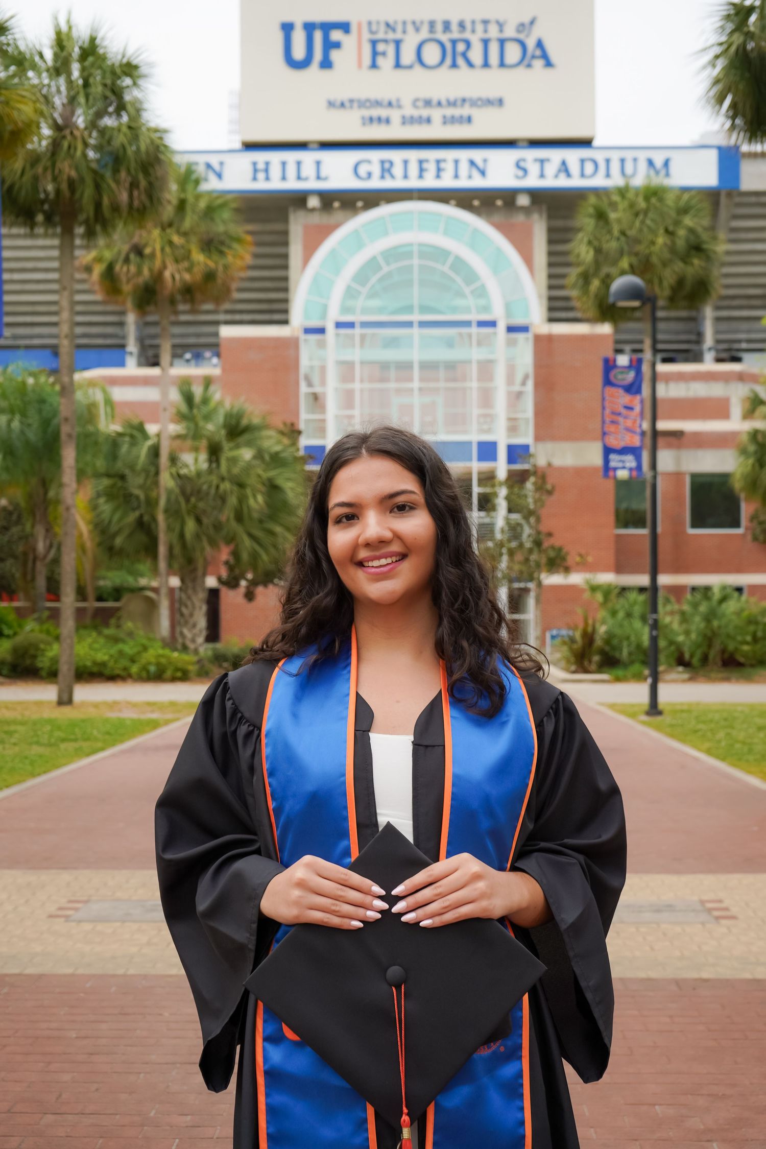 Graduate in cap and gown poses with blue and orange stole at UF stadium.