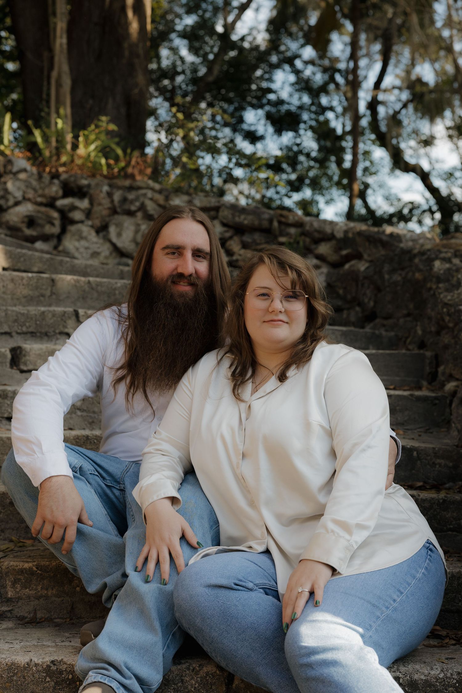 A casual couple's photoshoot on stone steps in matching white tops and blue jeans.