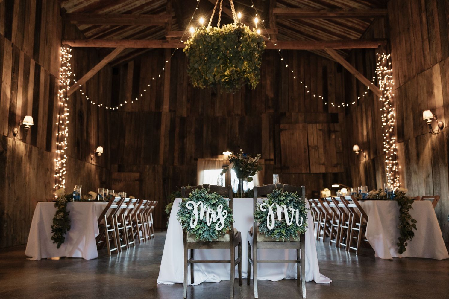 Rustic barn wedding venue interior decorated with string lights and white draping.