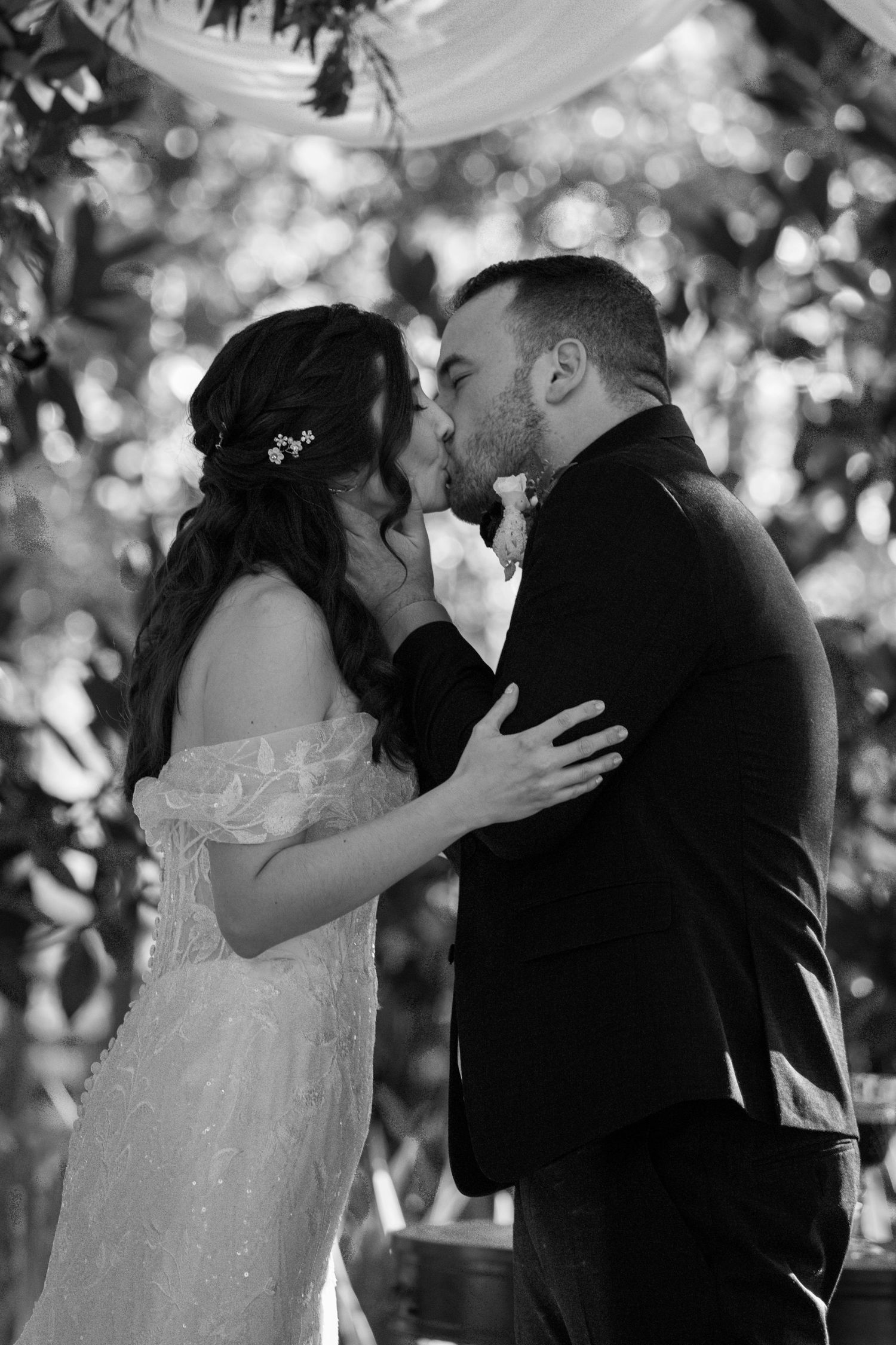 Black and white wedding photos capture couple sharing their first kiss as newlyweds.