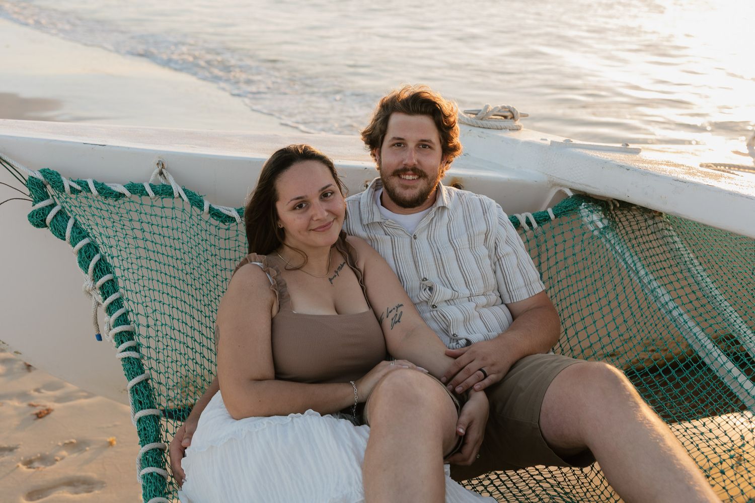 Couple smiling together on a beach hammock at sunset, relaxing by the ocean shore.
