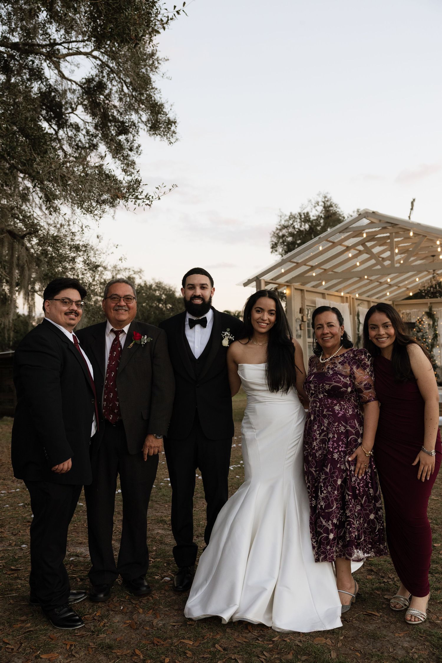 Wedding party poses together under a wooden pergola at sunset.