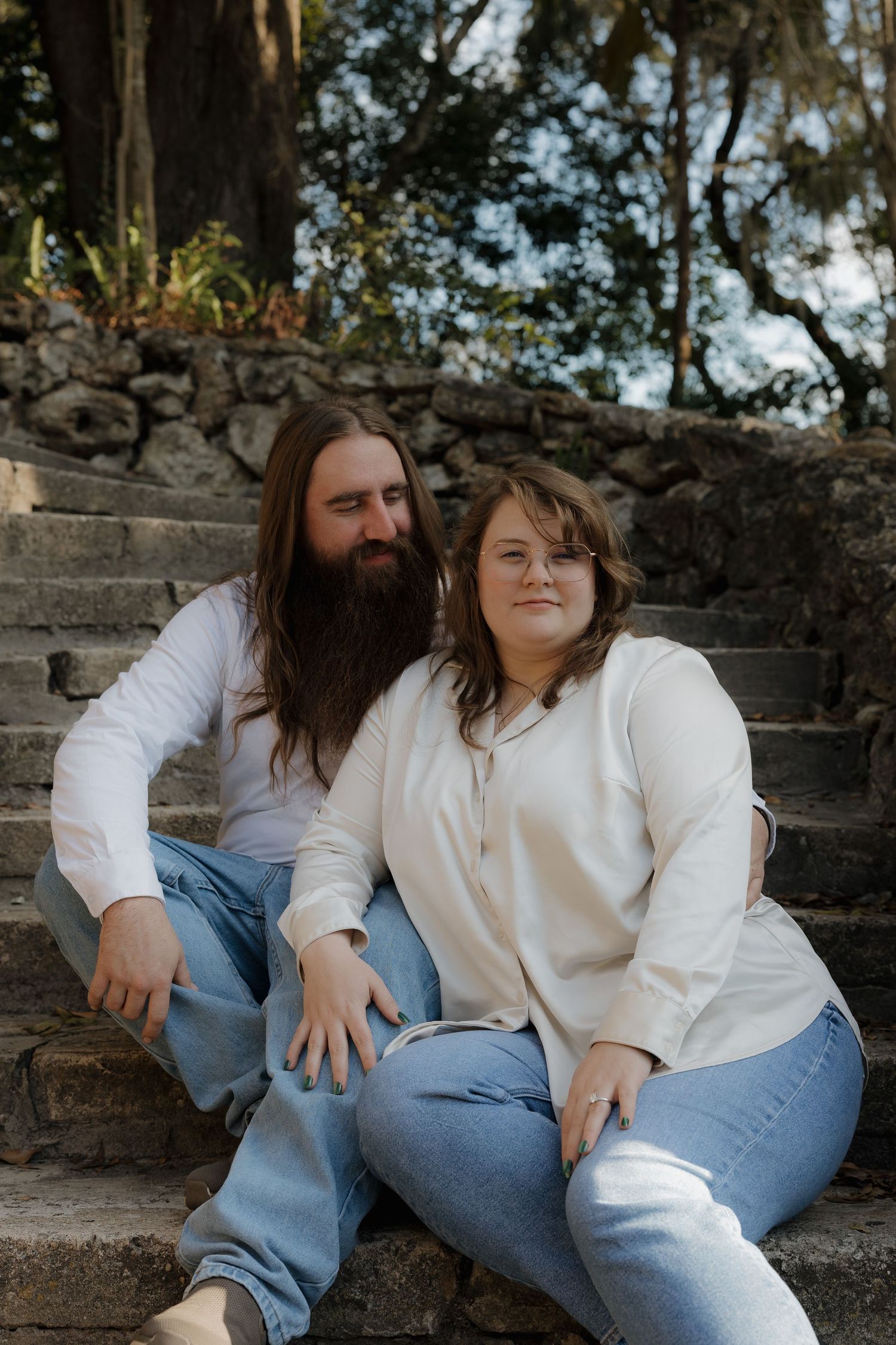 Casual couple in white tops and jeans sitting together on stone steps outdoors.