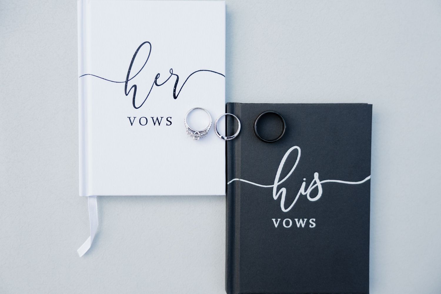 Minimalist white and black wedding vow books arranged on a light gray background.