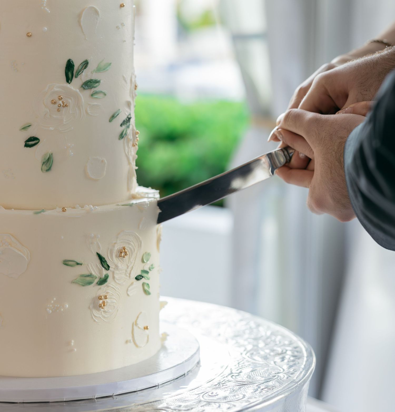 Elegant white wedding cake with floral details being cut with a knife by a person in formal attire.