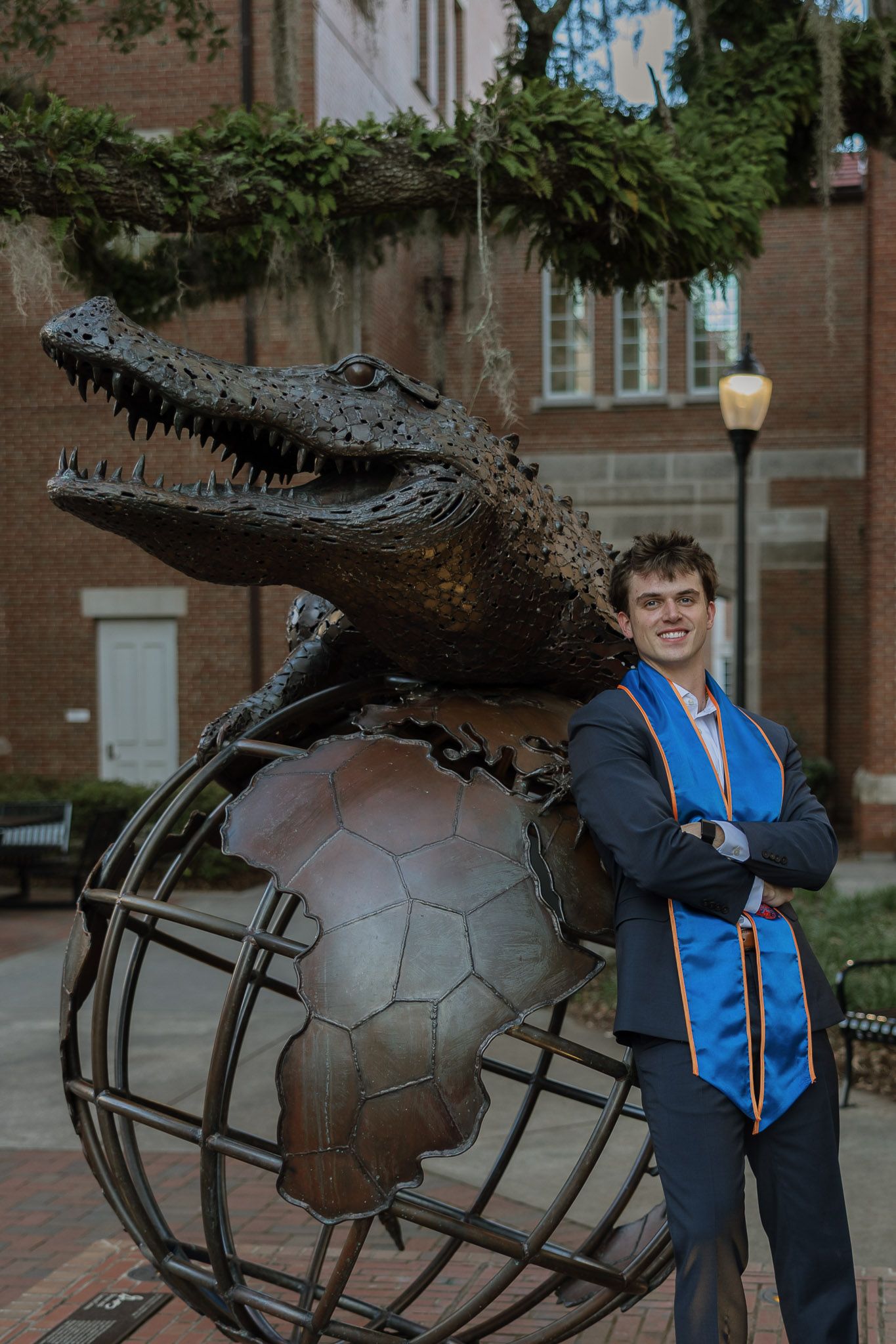 Graduate in blue stole poses beside Albert the Alligator bronze statue on globe at University of Florida campus.