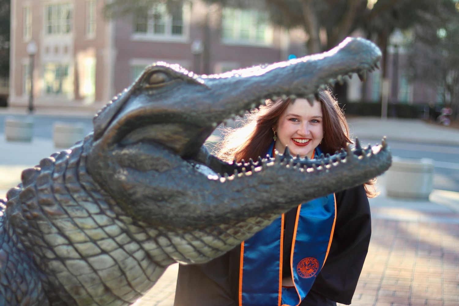 Student takes graduation photos with University of Florida alligator statue in blue graduation stole.