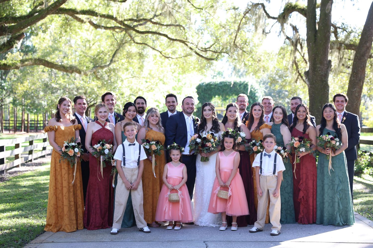 Large wedding party group photo with mixed autumn-colored attire.
