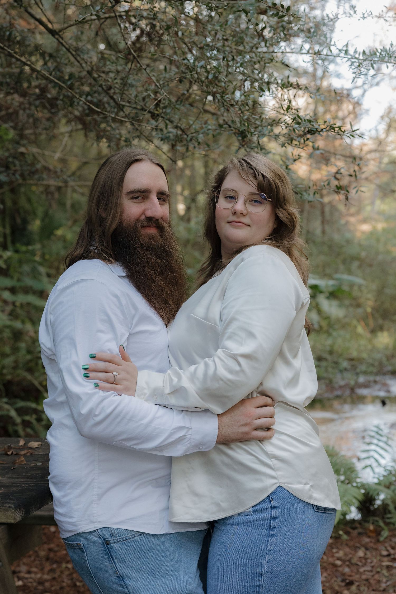 Couple in white tops embracing outdoors among autumn trees and foliage.