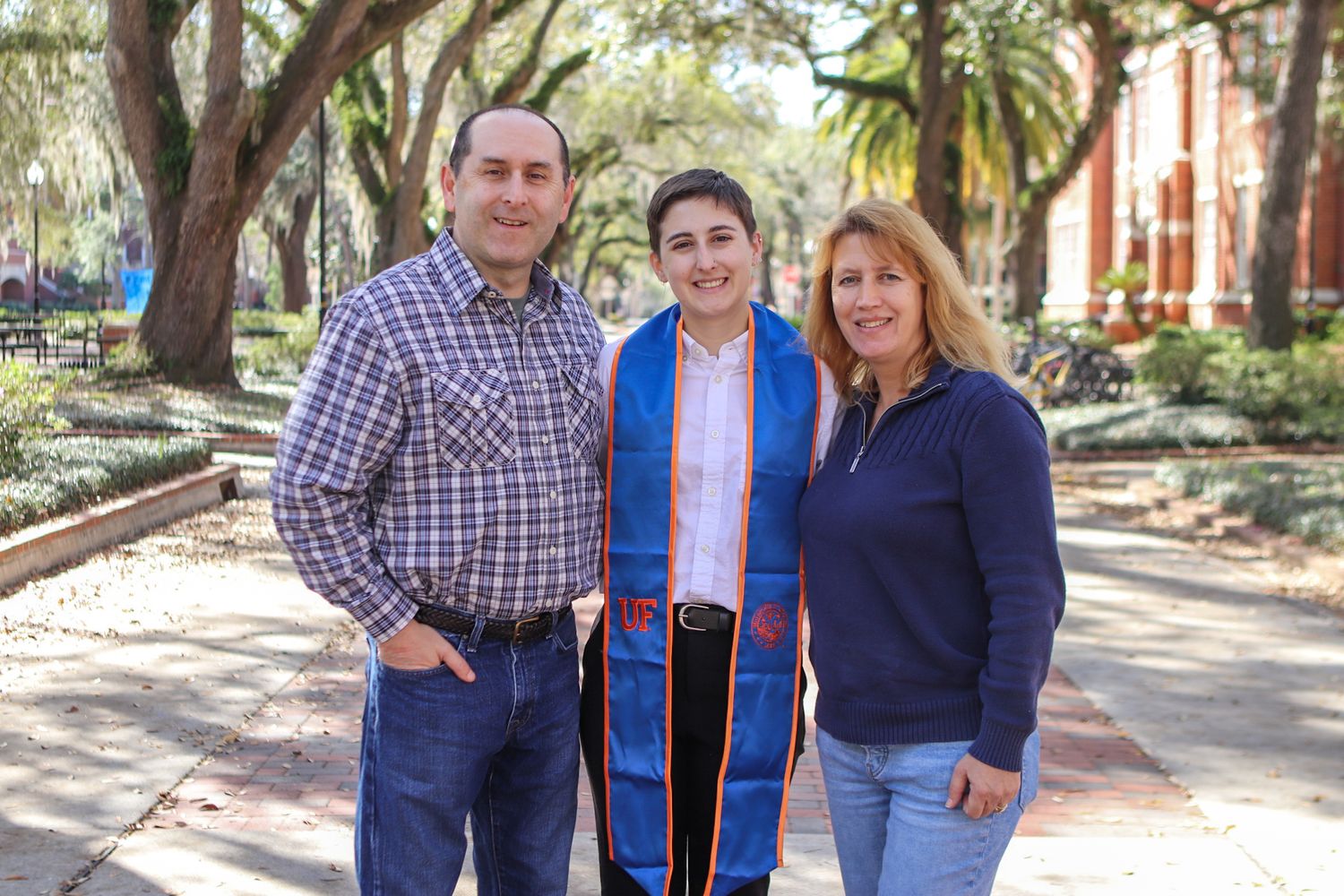 Family poses together on tree-lined campus walkway during graduation celebration.