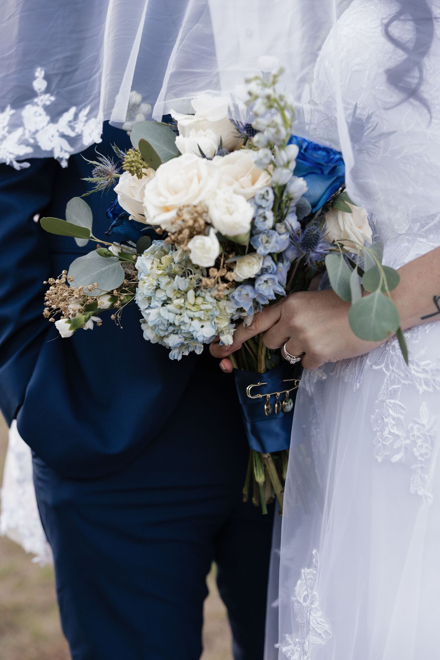 Wedding bouquets featuring white roses, blue flowers, and eucalyptus against navy and white attire.