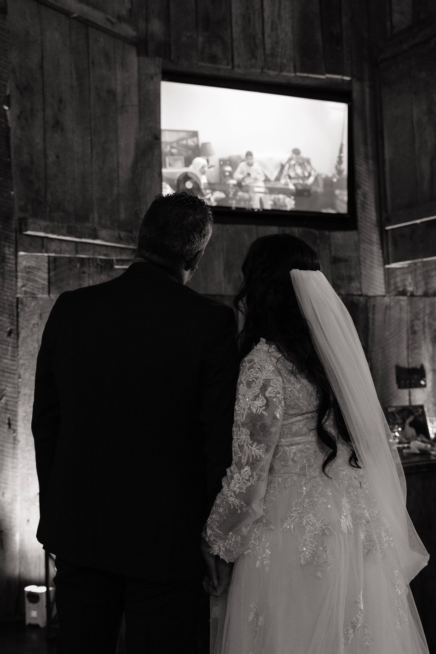 Silhouetted figures in wedding attire inside a rustic barn setting.