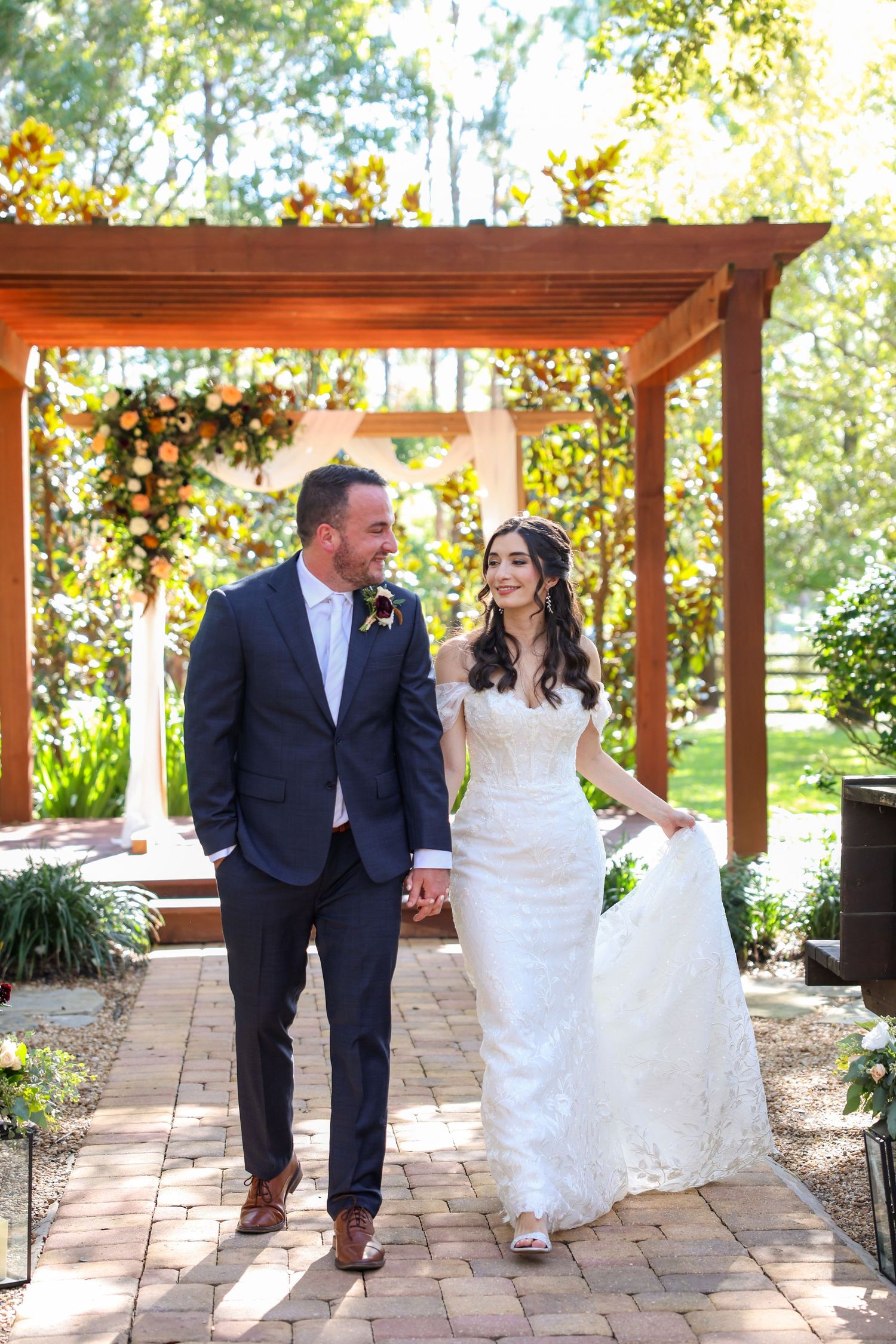 Newlyweds share playful moments on stone patio under wooden pergola.