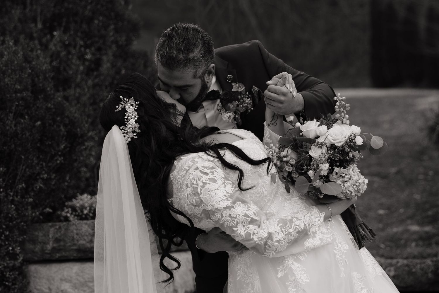 Wedding couple embracing outdoors in dramatic black and white photography.