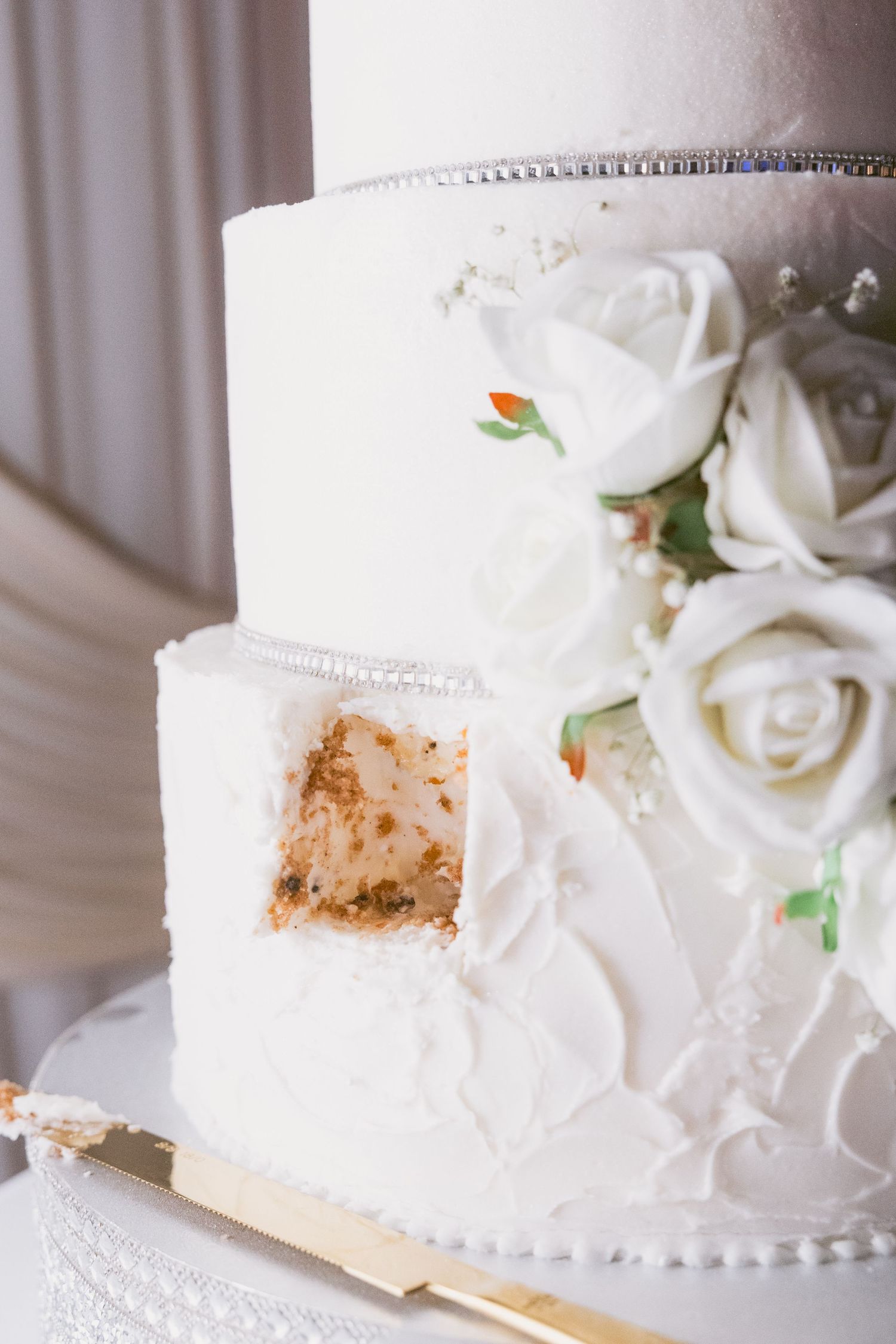 Elegant white wedding cake decorated with delicate roses and pearl details.