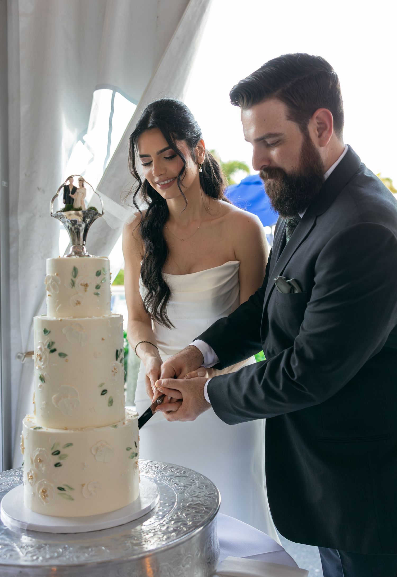 Bride and groom cutting a white four-tier wedding cake topped with a figurine at their wedding reception.