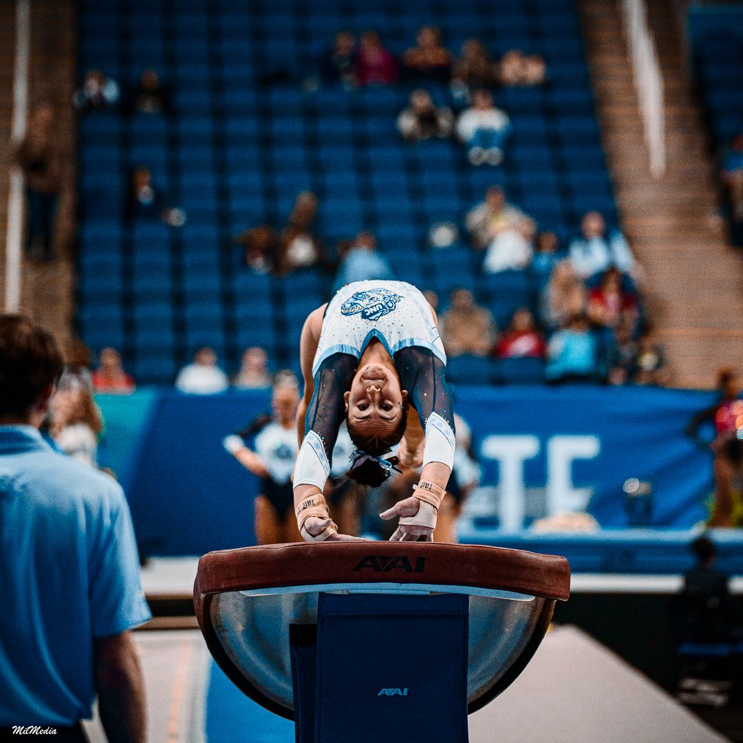 Athlete performs handstand on vault during gymnastics competition.